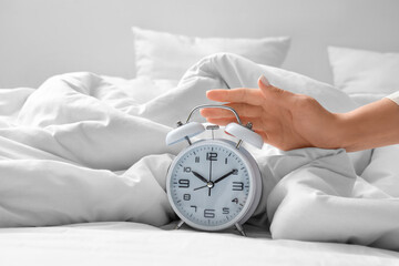 Young woman turning off alarm clock on bed in bedroom, closeup