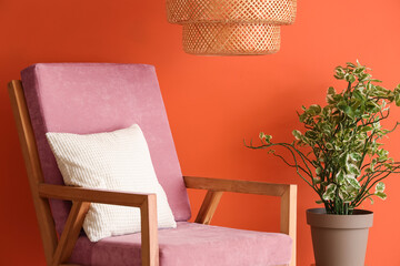 Pink armchair and houseplant near orange wall in room, closeup