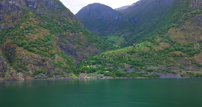 Majestic green cliffs and deep blue fjord waters under cloudy skies, filmed from a cruise ship sailing through the breathtaking landscapes of Norway fjords.