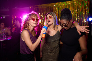 Young women singing karaoke and having fun at nightclub