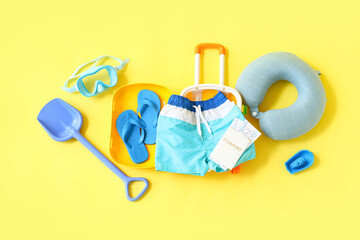 Suitcase with children's swimming trunks, passport and beach accessories on yellow background