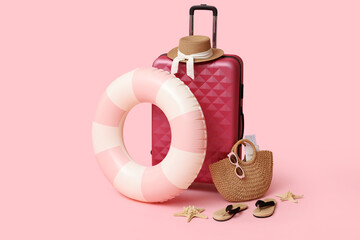 Suitcase, inflatable ring and beach accessories on pink background