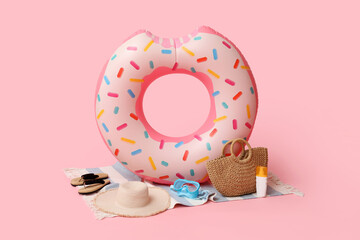 Inflatable ring in shape of donut, bottle of sunscreen cream and beach accessories on pink...