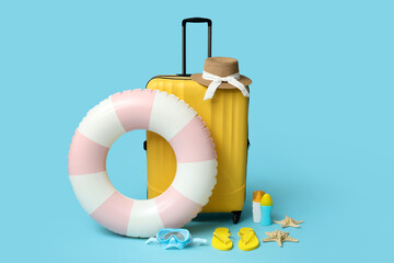 Inflatable ring, suitcase, bottles of sunscreen cream and beach accessories on blue background,...