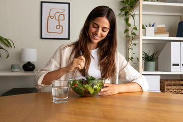 Young caucasian woman eating healthy salad at home.