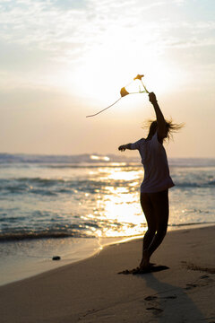 Woman dancing on the beach at sunset holding bikini top