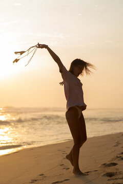 Woman dancing on the beach at sunset twirling her swimsuit in the wind