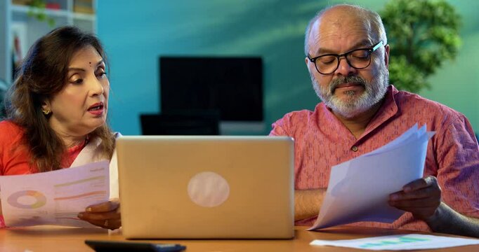 Indian couple managing home finance using laptop and documents, senior Asian husband wife reading bills calculating pension or taxes at home, planning retirement budget, digital paperwork concept - Powered by Adobe