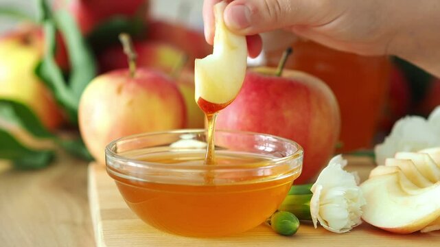 A child's hand dips an apple slice into honey. Rosh Hashanah. A family festive meal with traditional apples and honey on the table. Shanah Tovah.