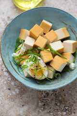 Smoked tofu cheese with soy-marinated egg and spring onion in a turquoise bowl, vertical shot, middle close-up