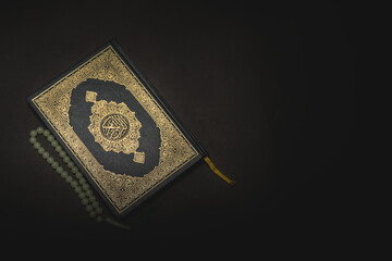Holy quran and prayer beads on dark background