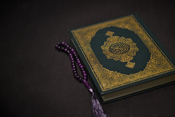 Holy quran and prayer beads on dark background