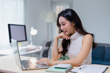 Focused young woman working on a laptop in a modern office setting. She is engaged in her task,...