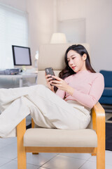 Young woman lounges comfortably in a modern living room, engrossed in her smartphone. The setting...