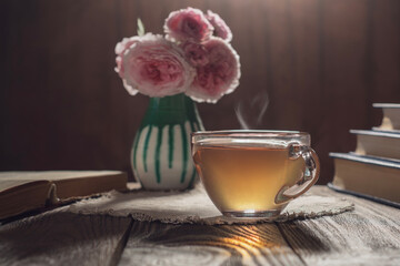 A transparent cup of black tea on a mottled brown background, standing on a table with books and a...