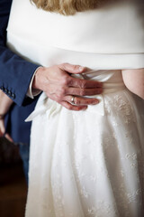Close up of a grooms hand hugging the bride in white dress, back view