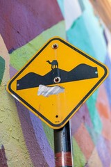A yellow road sign, with a camel sticker, warns drivers. The sign is mounted in front of a colorful...