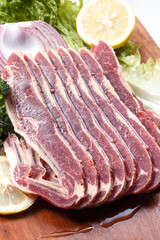 Beef ribs with lemon, onion and lettuce on a wooden cutting board