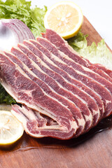 Beef ribs with lemon, onion and lettuce on a wooden cutting board