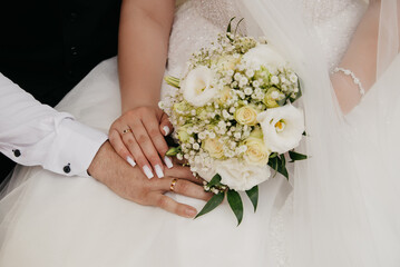 The bride's hand with a gold wedding ring lies on the groom's hand, both hands lie on the wedding...