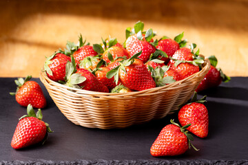Fresh strawberries in a wicker basket on a dark slate board under warm light. Juicy and ripe red berries perfect for food and nutrition concepts