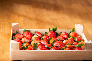 Ripe strawberries in a rustic wooden crate on a wood table. Studio lighting highlights the vibrant red color and freshness of the berries.