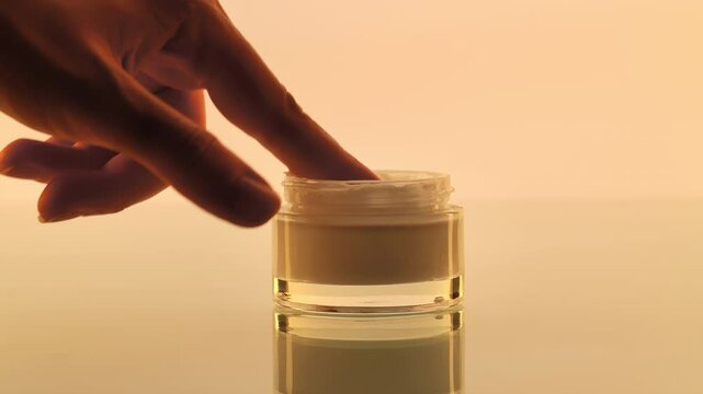 Hand Dipping Finger in Skincare Cream Jar Close-Up Image