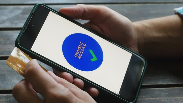 Person paying online using smartphone and bank credit card. Payment received text on mobile phone screen. 