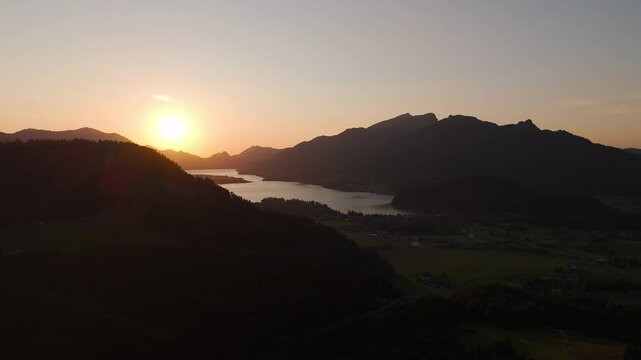 Drone view of vibrant sunset over lake Wolfgangsee and the village of Strobl in Austria, sun&rsquo;s warm glow silhouettes distant mountains and reflects on the calm lake.