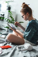 Young freelancer girl concentrates on designing colorful illustration on digital tablet. Cozy...