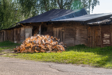 Pile of Firewood Logs Stacked Outside Rustic Wooden Shed in Rural Countryside. Freshly Cut Firewood Near Old Barn on Sunny Summer Day in Village Setting

.