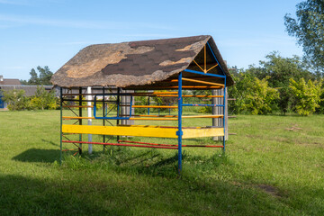 Colorful Outdoor Playground Shelter in Green Countryside Field on Sunny Summer Day. Rustic Children's Play Area with Painted Metal Structure in Rural Village Setting