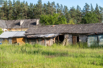 Abandoned Outbuildings with Overgrown Grass and Tiled Roofs in Rural Village. Dilapidated Brick and...
