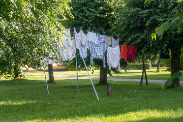 Colorful laundry hanging to dry between trees in green courtyard of Soviet-style apartment block on a sunny summer day in Eastern Europe, simple life, authentic rural lifestyle