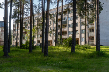 Soviet-era apartment building in Eastern Europe seen through tall pine trees on a sunny summer day,...