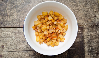 delicious stir-fried diced potatoes with spicy seasoning in white bowl on wooden table. Flat lay