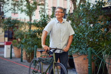 Senior man walkimg with bicycle on city street