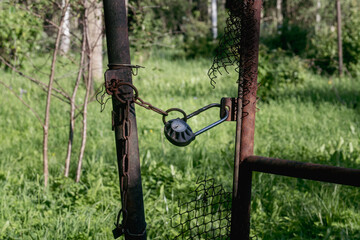 Old rusty chain and padlock securing broken metal gate in overgrown forest field, symbolizing...