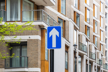 Blue one way traffic sign with upward arrow on modern city street near contemporary flats