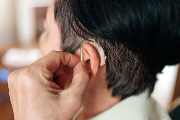 Fototapeta premium Close-up of a senior woman adjusting her hearing aid, showcasing healthcare support, assistive hearing technology, and daily independence solutions for aging and hearing-impaired individuals.
