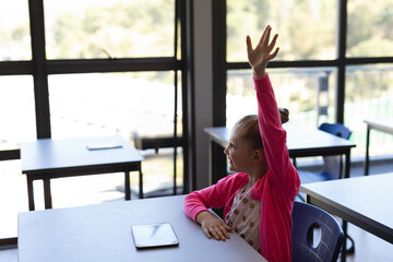 Tablet is resting on classroom desk amid tidy rows of student chairs near bright windows