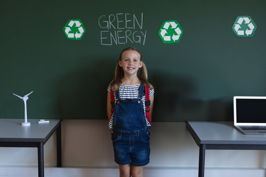 Girl standing in classroom by green board with GREEN ENERGY text, recycle icons, turbine, laptop - Powered by Adobe