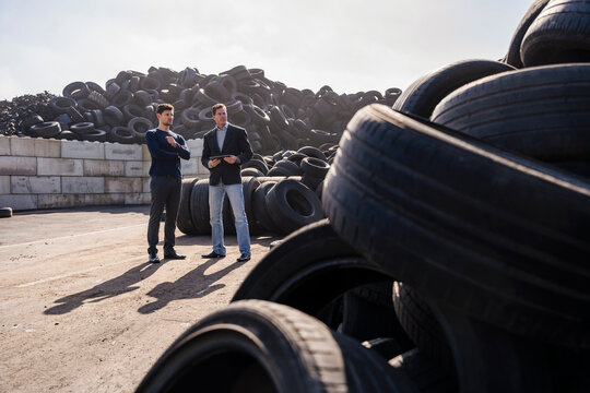 Businessmen discussing over rubber tires at recycling plant on sunny day - Powered by Adobe