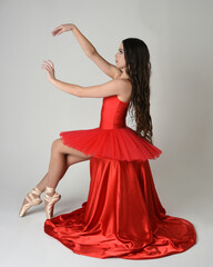 female ballerina dancer model, graceful seated pose on red silk chair, stretching with graceful arms. wearing classical ballet red tutu and pointe shoes costume on white isolated studio background