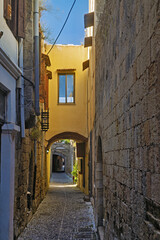 Fototapeta premium narrow alleyway paved with stone tiles and flanked by aged stone and stucco buildings stone arches span across the alley overhead in old town of Rhodes, Greece