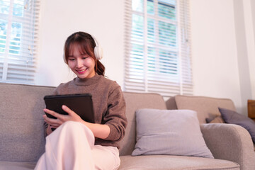 Asian Woman Relaxing Home Integrating AI Technology Enjoying Digital Content on Tablet with Headphones for Enhanced Daily Life
