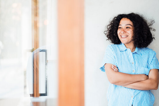 Cheerful woman with arms crossed standing in front of wall