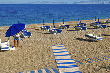 Sunny and peaceful beach on the island of Rhodes, Greece. The sand is golden and dotted with yellow...