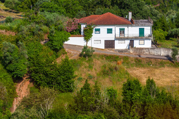 A white house with a red-tiled roof sits amidst lush greenery