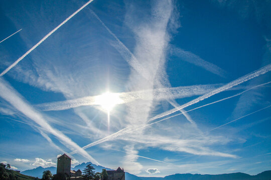 Dawn sky above the Alps streaked with dense contrails — fresh white lines and faded trails crisscrossing endlessly. Abstract aviation patterns over Merano. South Tyrol, Italy.

